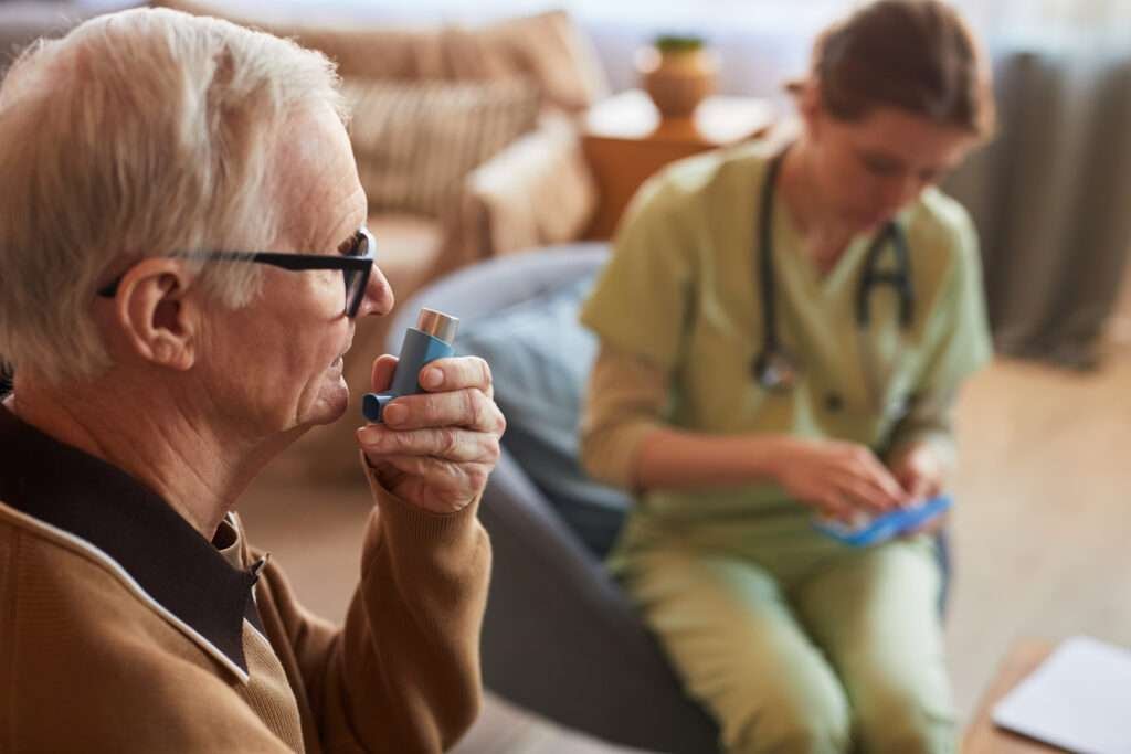 Older man using an inhaler to manage COPD while a nurse assists at home